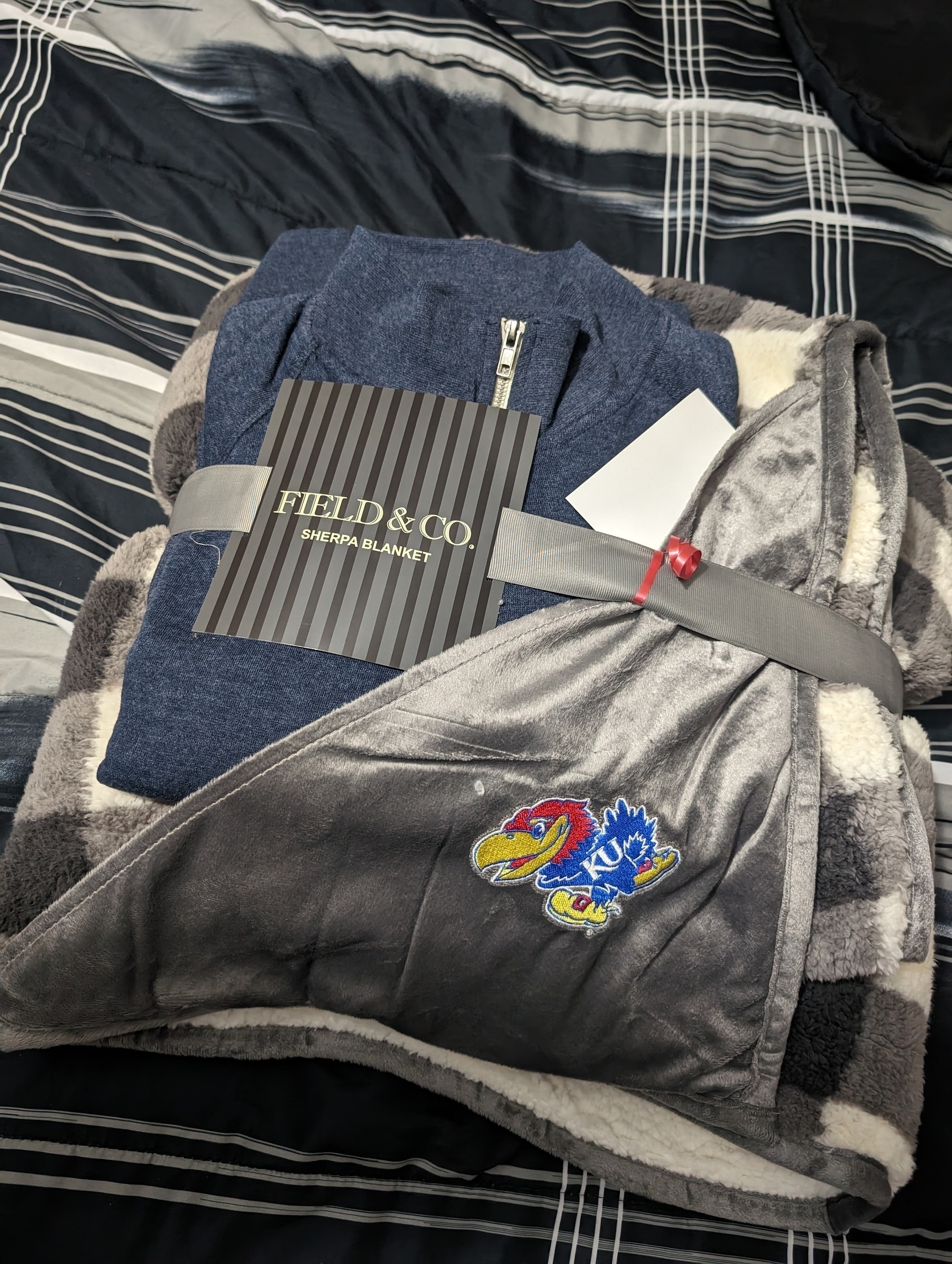 Photo of a blue quarter zipper sweater that is wrapped in a Field and Company fuzzy blanket that is embroidered with a Kansas University Jayhawk logo.