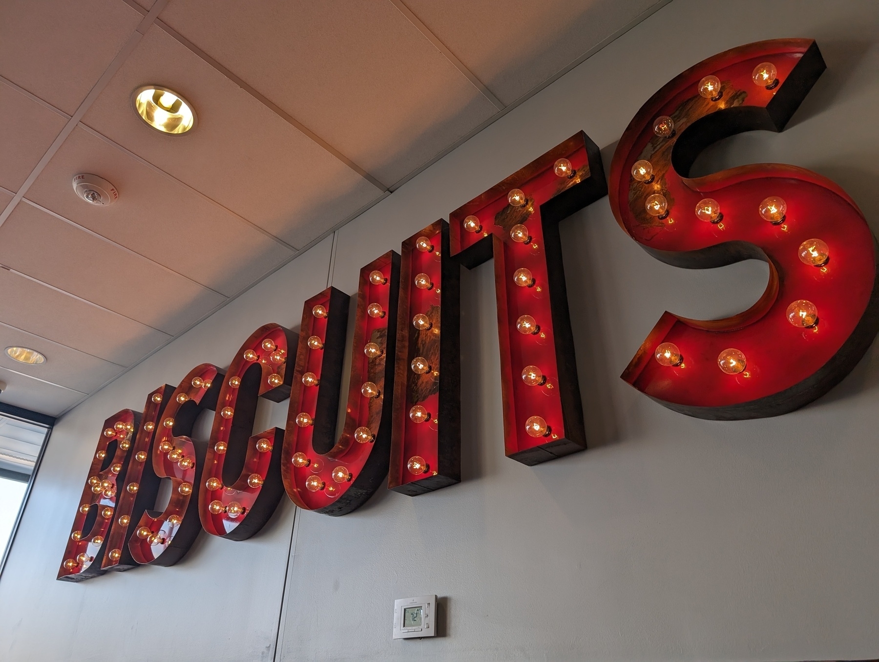 Photo of a sign built up of large letters, red with old school light bulbs inside. The letters spell out the word BISCUITS