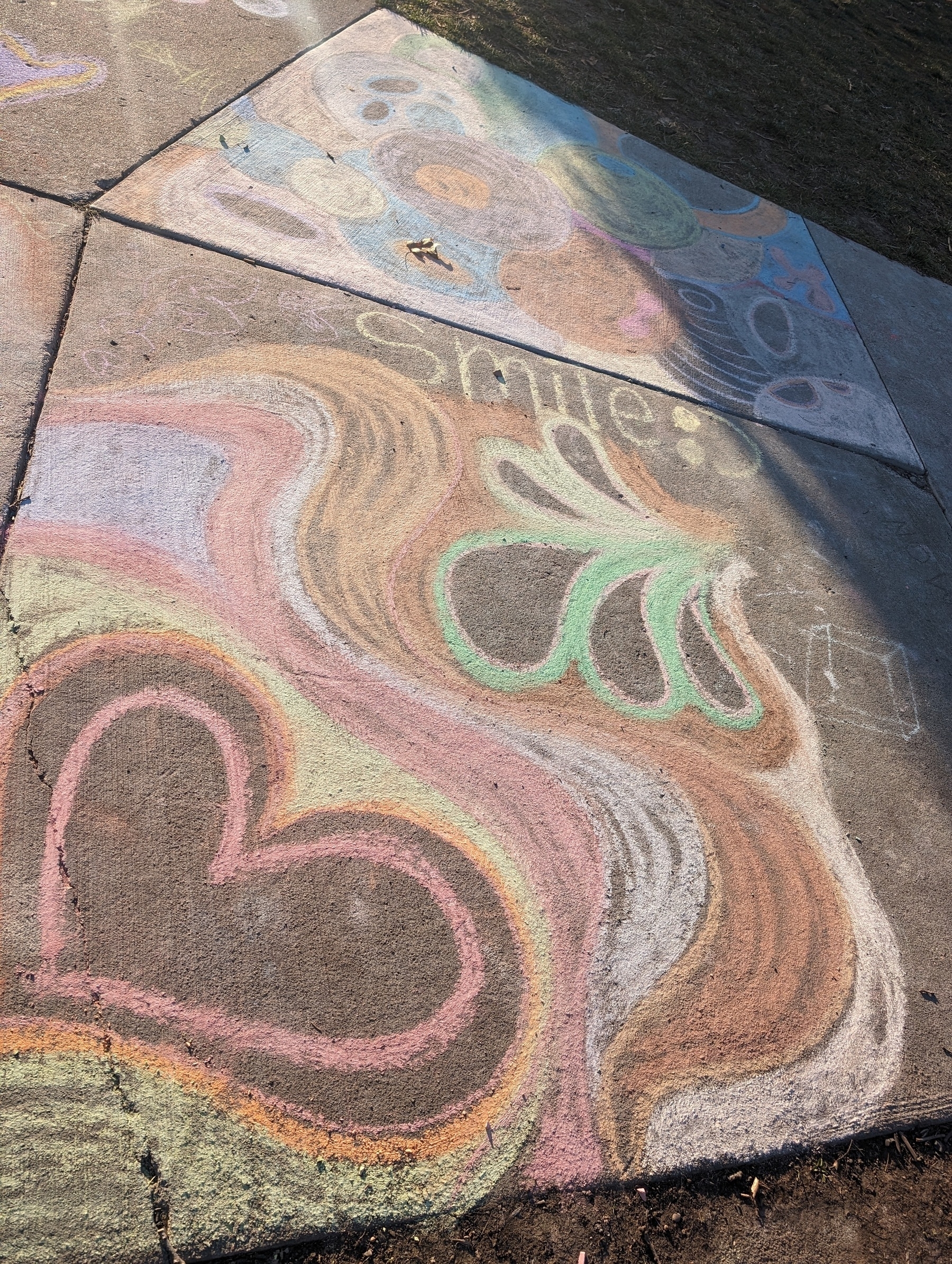 Photo of sidewalk chalk artwork. Colorful hearts, teardrop shapes, the word "smile".