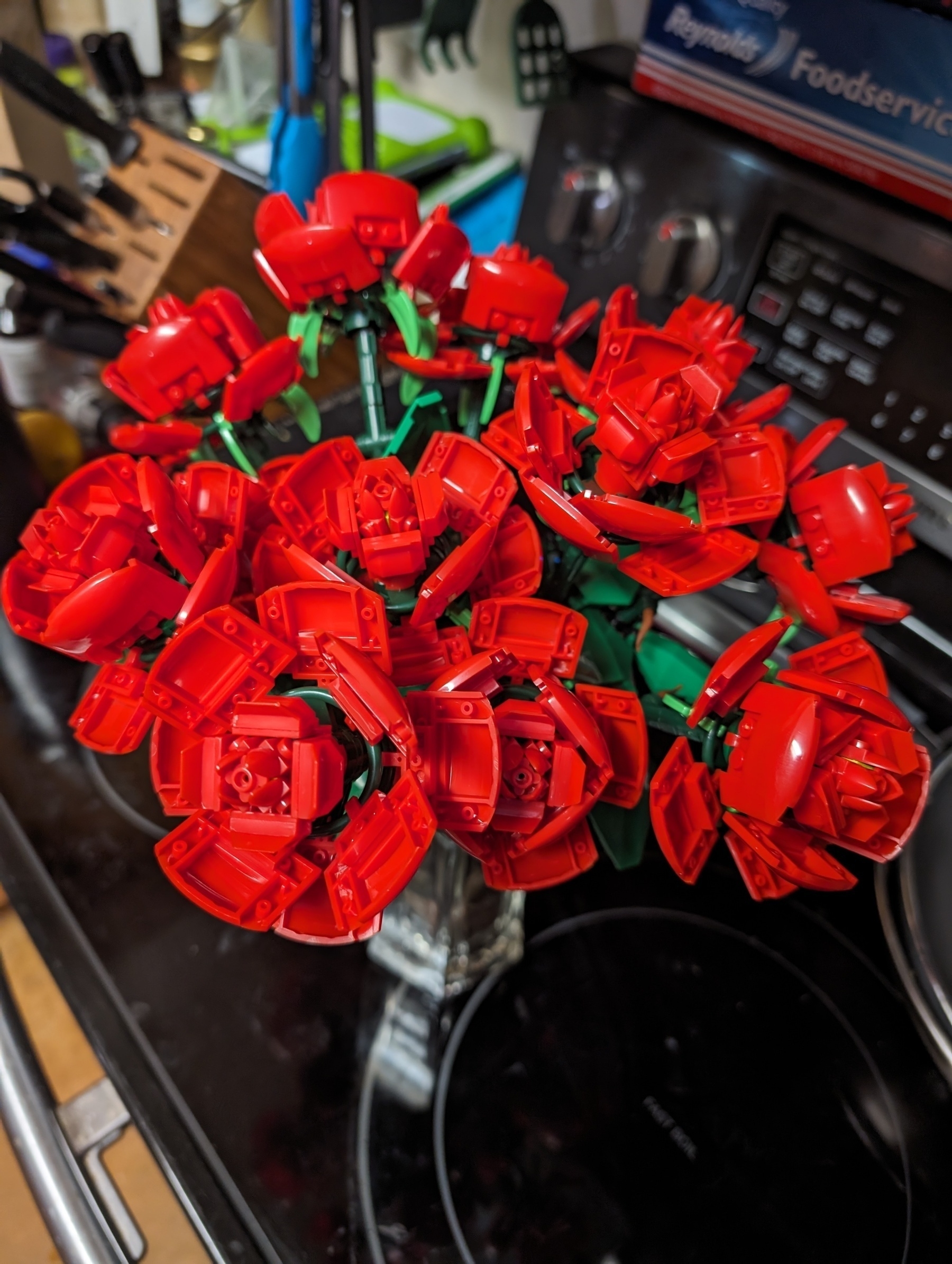 Photo of a dozen red roses built out of an interlocking brick building system. Displayed in a clear glass vase.