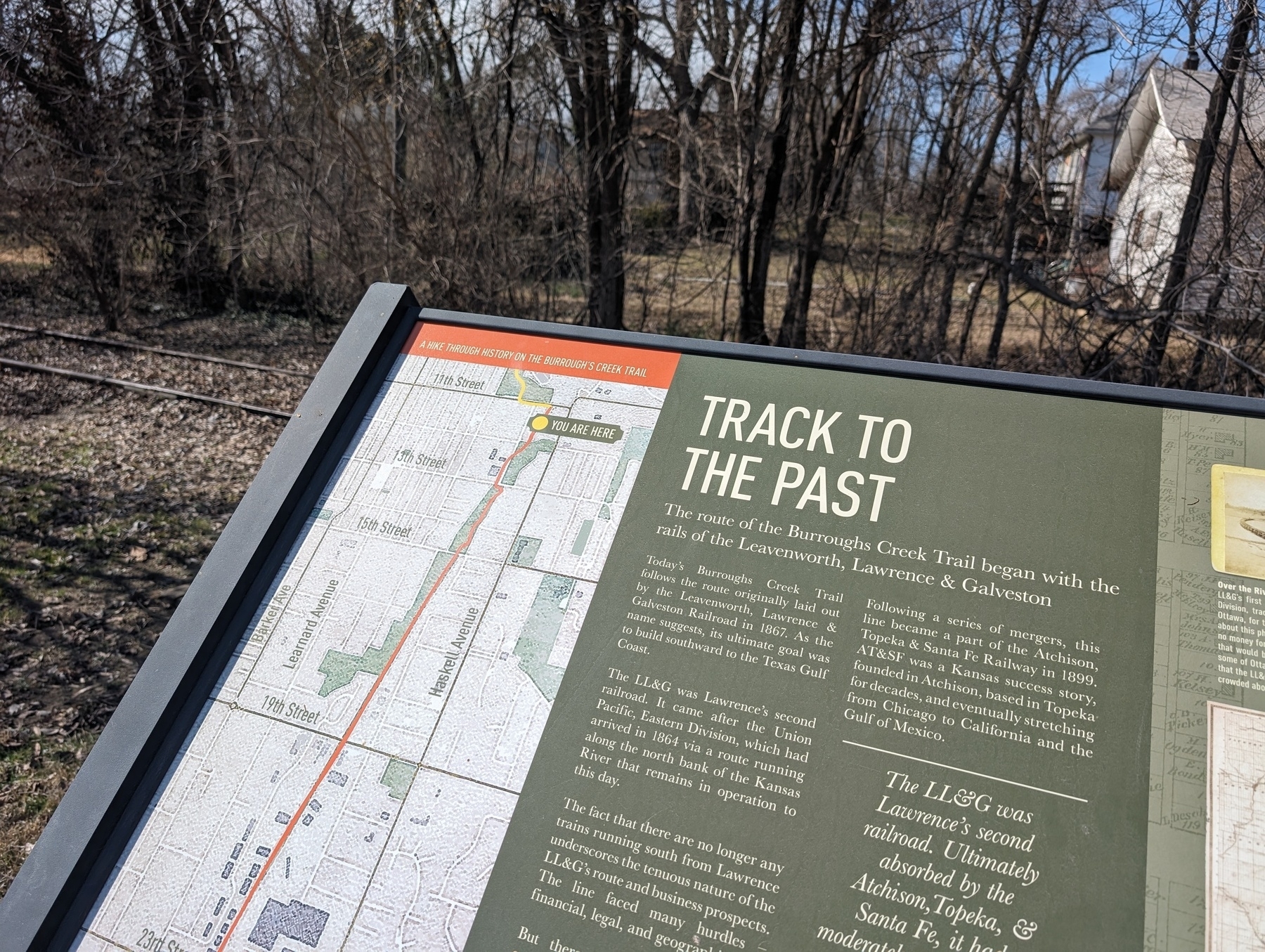 A photo of an information placard/marker placed along a local walking trail. The marker is titled "A Track To The Past". Along the left side is a map that indicates the location. 